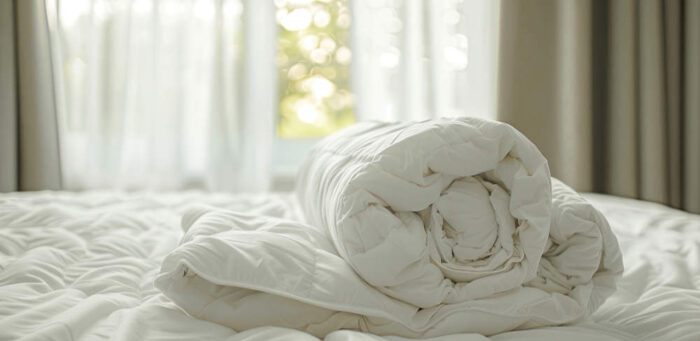 Cozy white folded duvet lying on white bed background. Preparing for winter season, household, domestic activities.